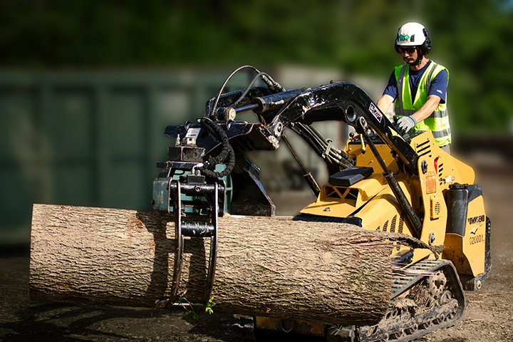 A man using a piece of equipment to move a large piece of a tree.